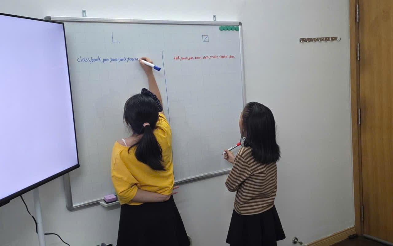 Hai bạn nhỏ lên bảng viết từ vựng tiếng Anh trong giờ học